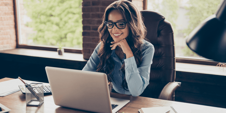 Woman at desk wearing glasses smiling looking at laptop reading article, Essential Keys to Selling More Mortgage Protection Policies