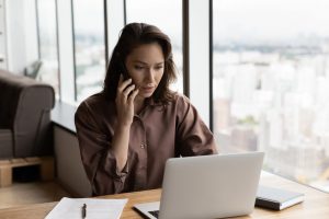 Woman sitting at desk on the phone looking at laptop selling life insurance in 2024