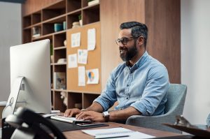 Man smiling at computer reading the article Running Paid Ads on Facebook vs. Google for Insurance Agents