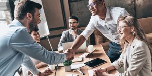 Insurance Agency with Agent at Desk with Two Members Shaking hands and smiling