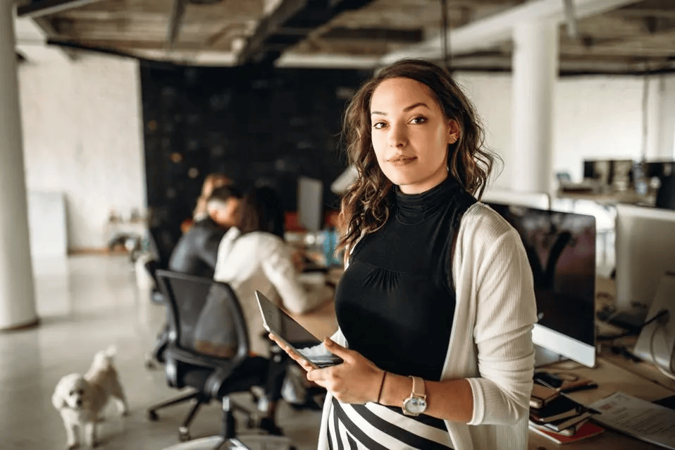 Successful Female Life Insurance Agency Owner Standing in Office with Team in Background Working